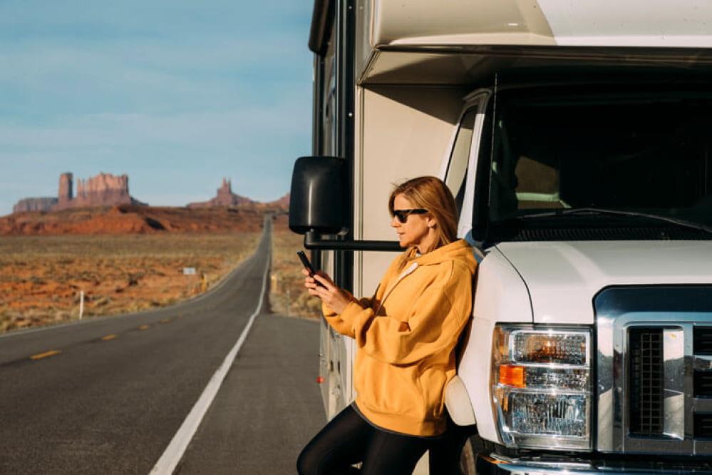 A person on their cell phone in front of an RV with a road in the background
